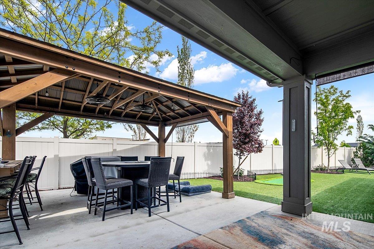 Covered patio featuring a wood-frame gazebo with a corrugated metal roof and integrated ceiling fans, a concrete paver surface, and a private fenced yard with artificial turf