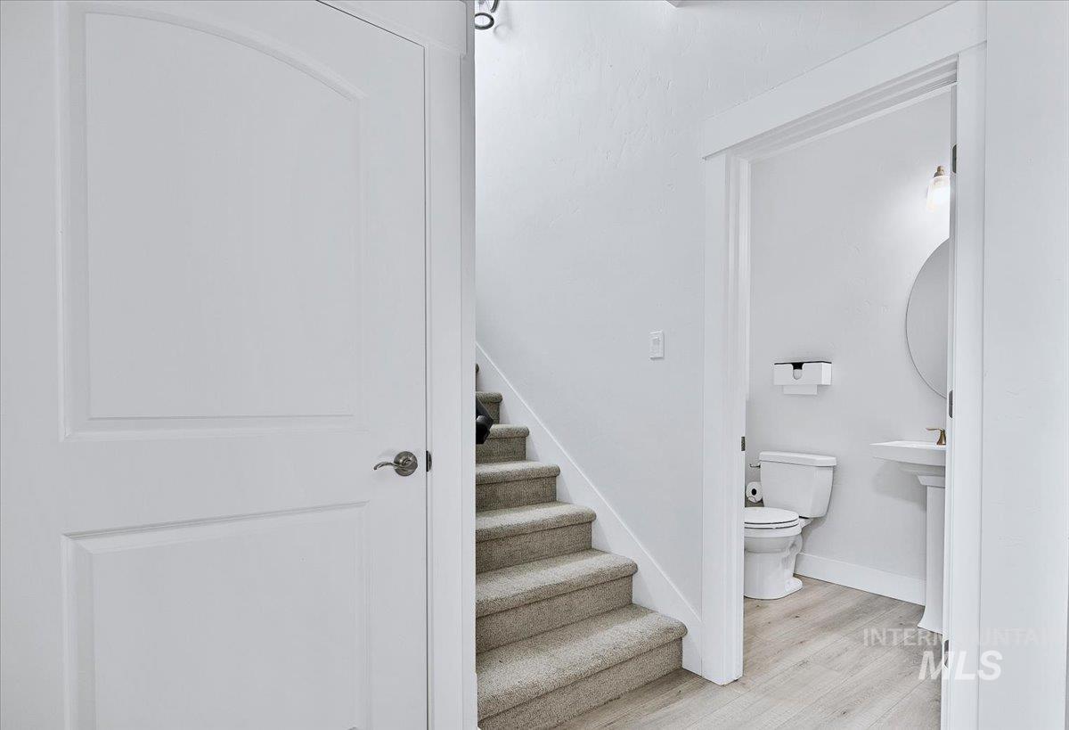 Ground floor powder room featuring a pedestal sink, round wall mirror, and light wood-finish flooring