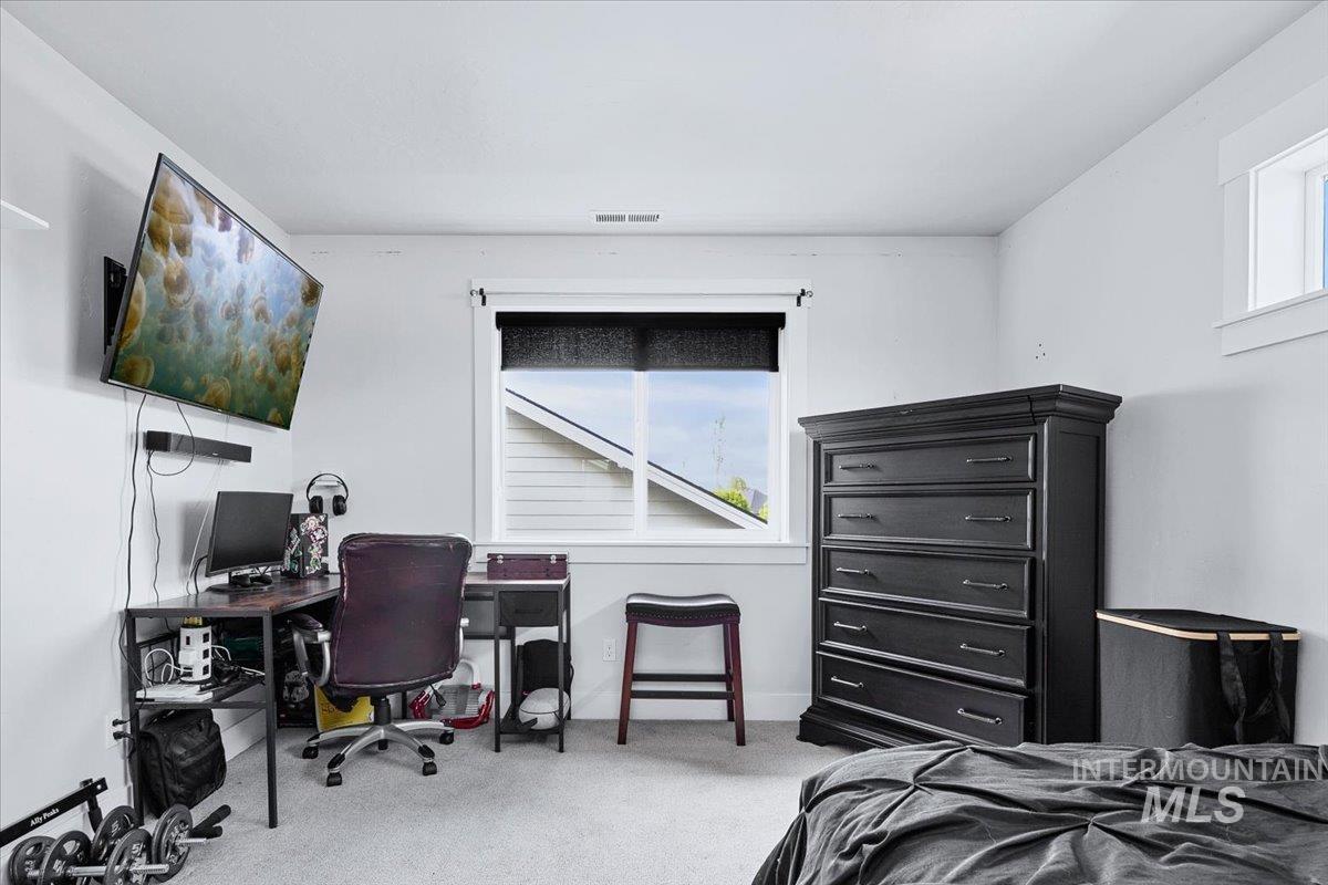 Carpeted room featuring a window with a roller shade, white walls, and a wall-mounted television