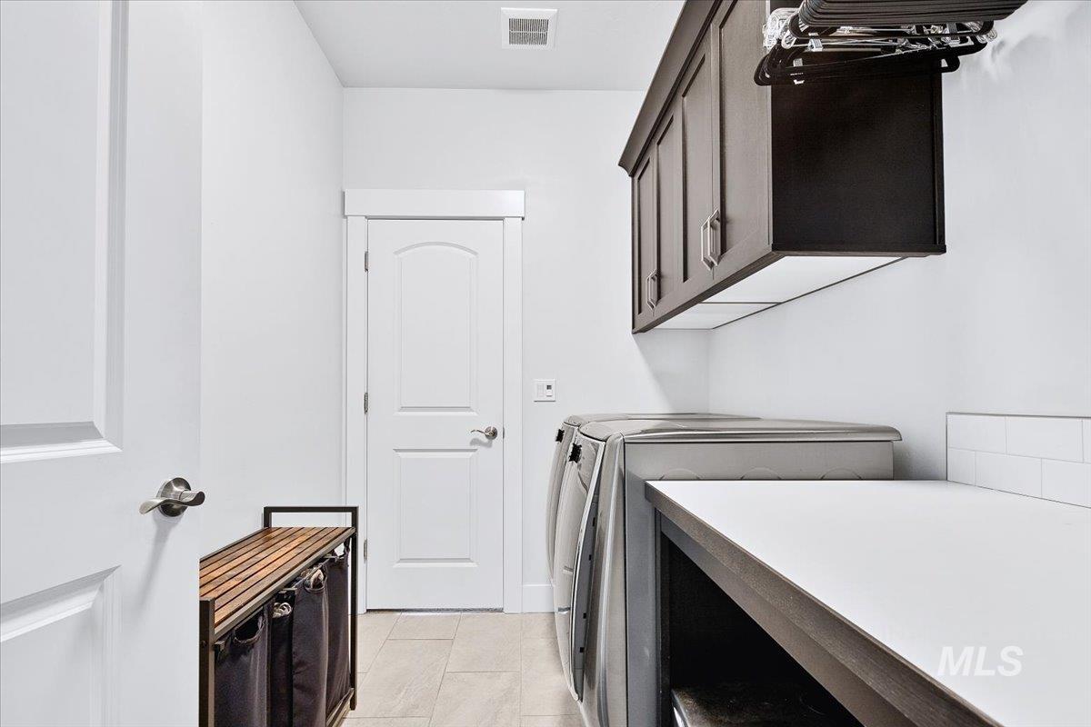 Laundry room featuring light tile flooring, white walls, dark upper cabinetry, a white countertop, and white subway tile backsplash