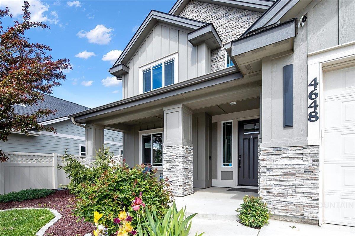 Modern exterior featuring a prominent stone facade, a covered front porch, vertical siding accents, and a dark entry door with a sidelight