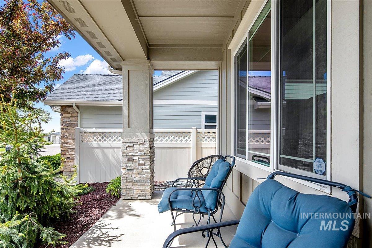 Covered concrete porch featuring a stone column, multiple windows, and landscaped plantings