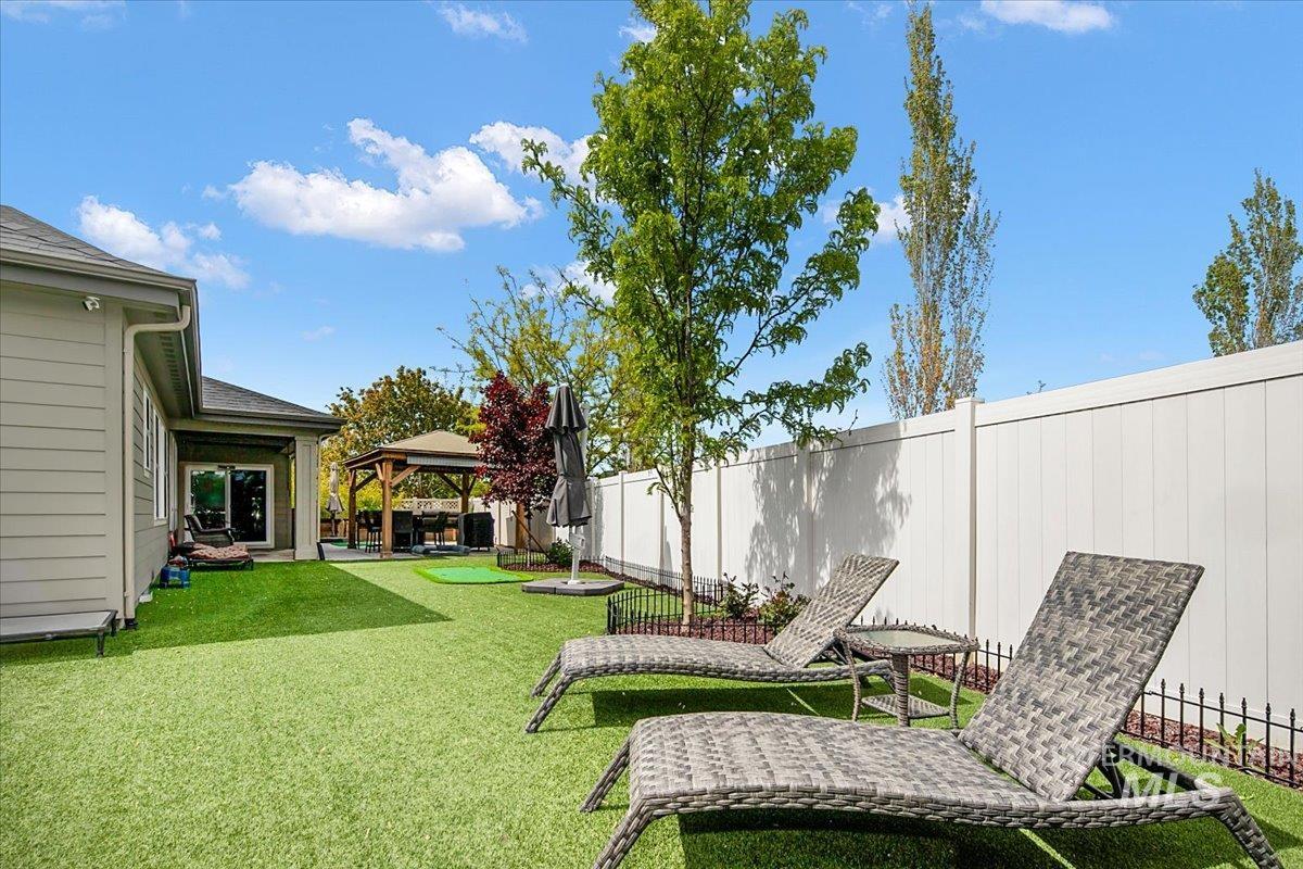 Spacious backyard featuring artificial turf, a white privacy fence, a covered patio with a sliding glass door, and a built-in gazebo