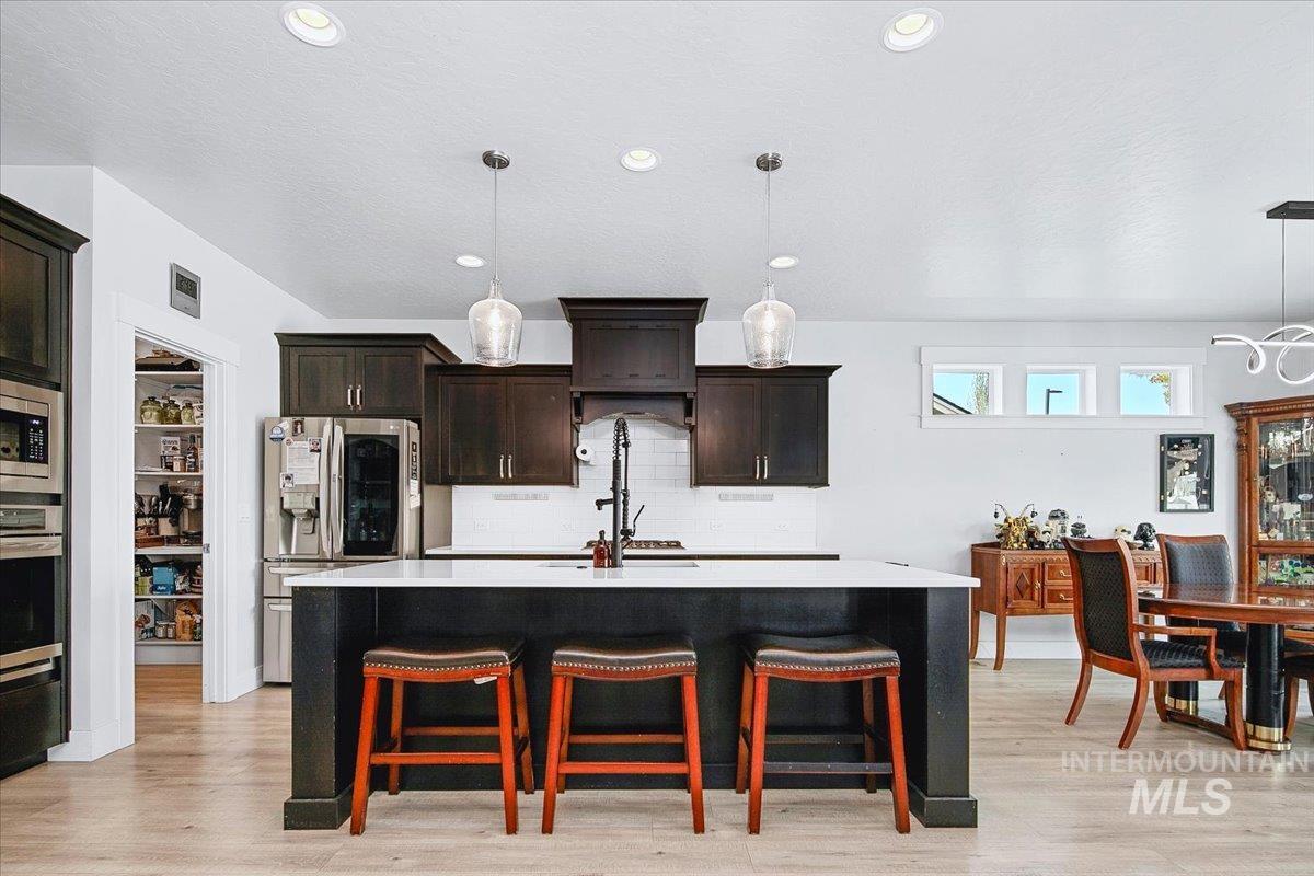 Spacious kitchen featuring an expansive center island with seating, dark wood cabinetry, stainless steel appliances, and wood-finish flooring