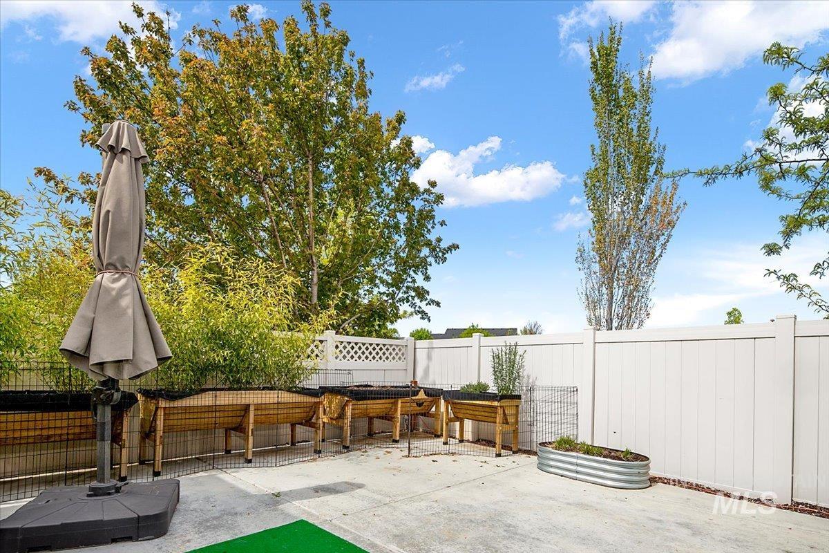 Outdoor patio space featuring a concrete surface, a white privacy fence, and multiple raised garden beds
