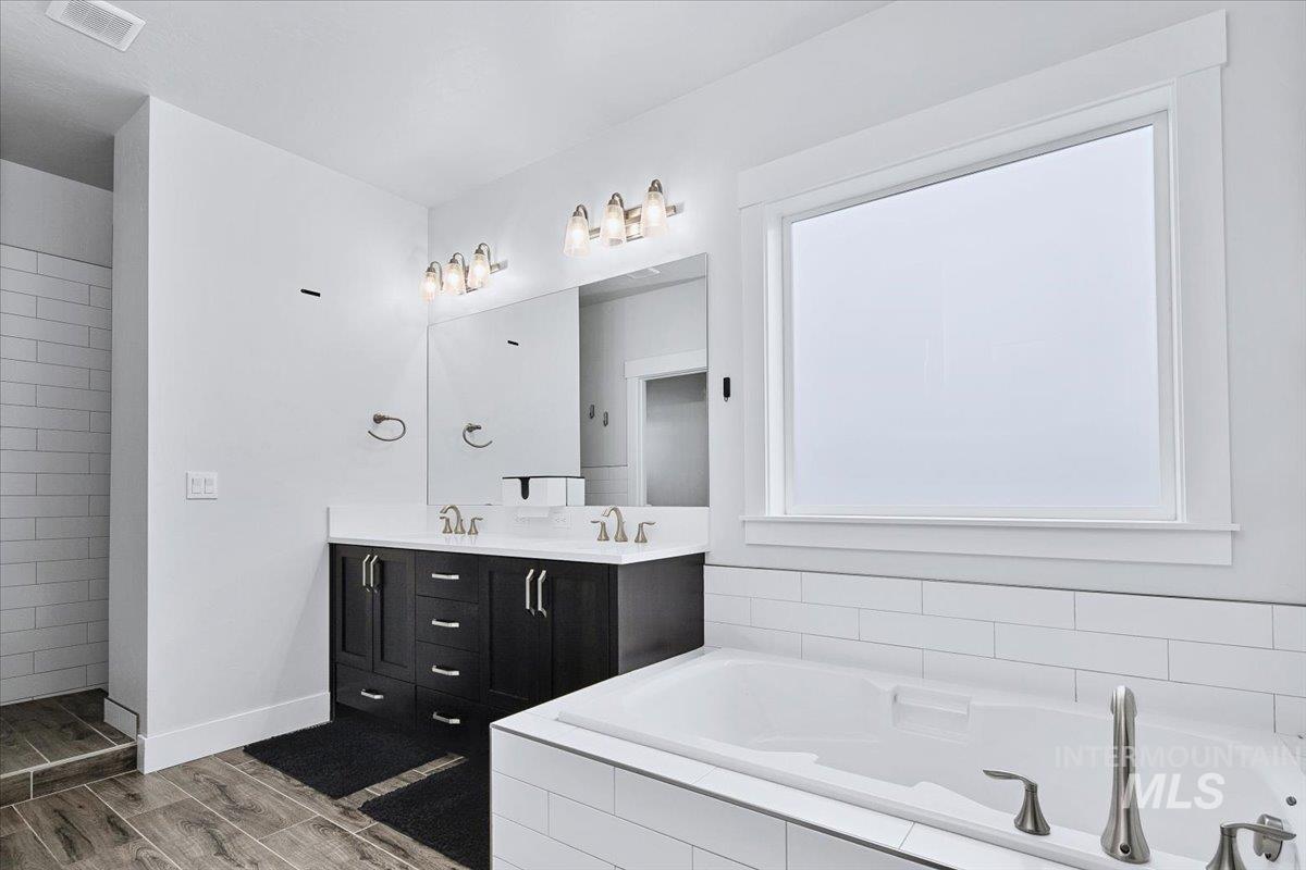 Soaking tub with brushed nickel fixtures, surrounded by white subway tile, and a large window with white trim