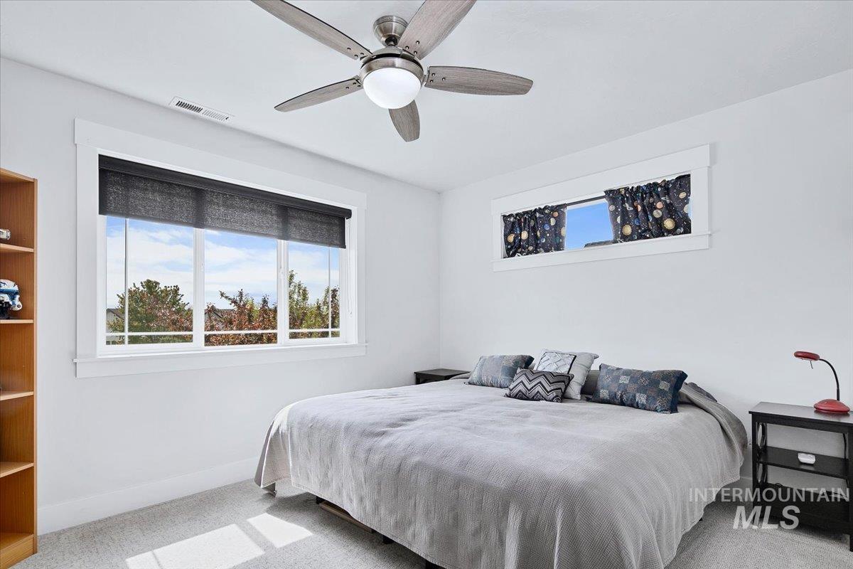 White walls with a ceiling fan light fixture, large multi-pane window with dark roller shade, and a high horizontal window