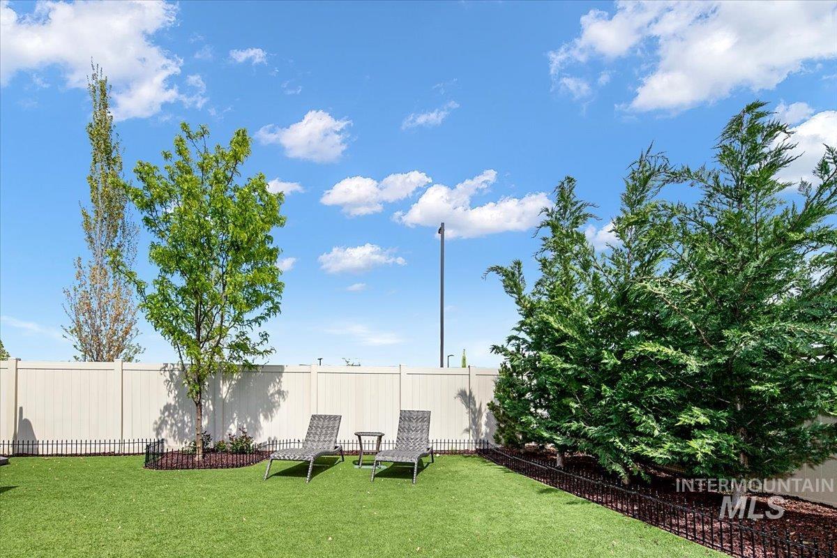 Green space featuring artificial turf, a light-toned privacy fence, mature trees, and decorative landscaping