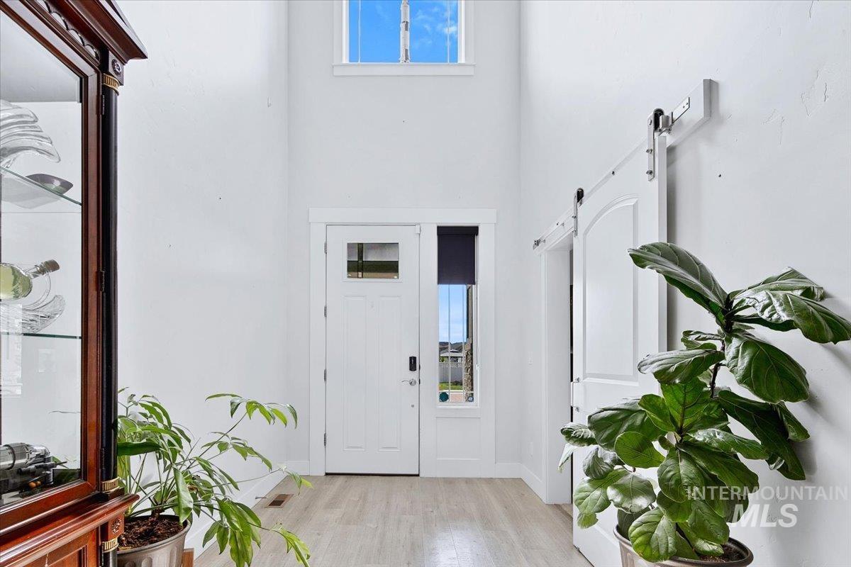 Two-story entryway featuring wood-finish flooring, a white paneled front door with sidelight and transom windows, and a white barn door with an arched top