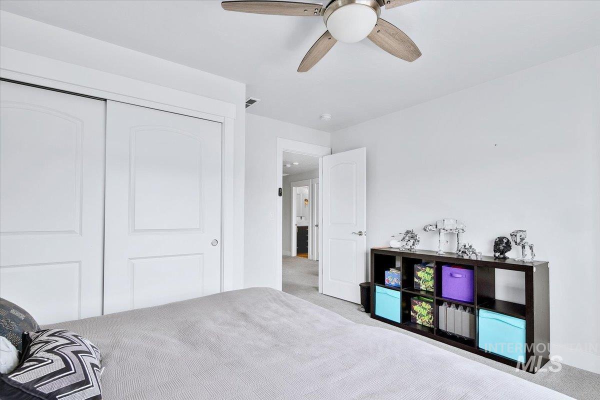 Bedroom featuring a ceiling fan with light fixture, white walls, and light-toned carpeting