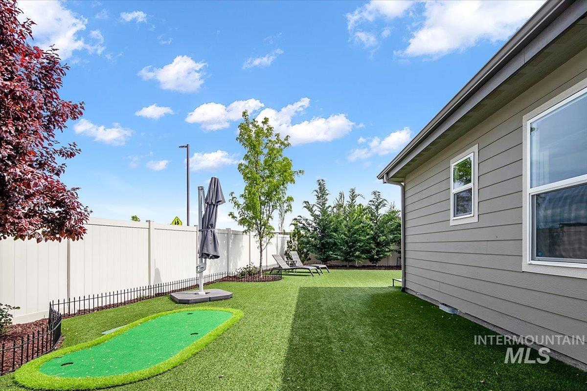 Expansive backyard featuring a putting green, artificial turf, and a white privacy fence