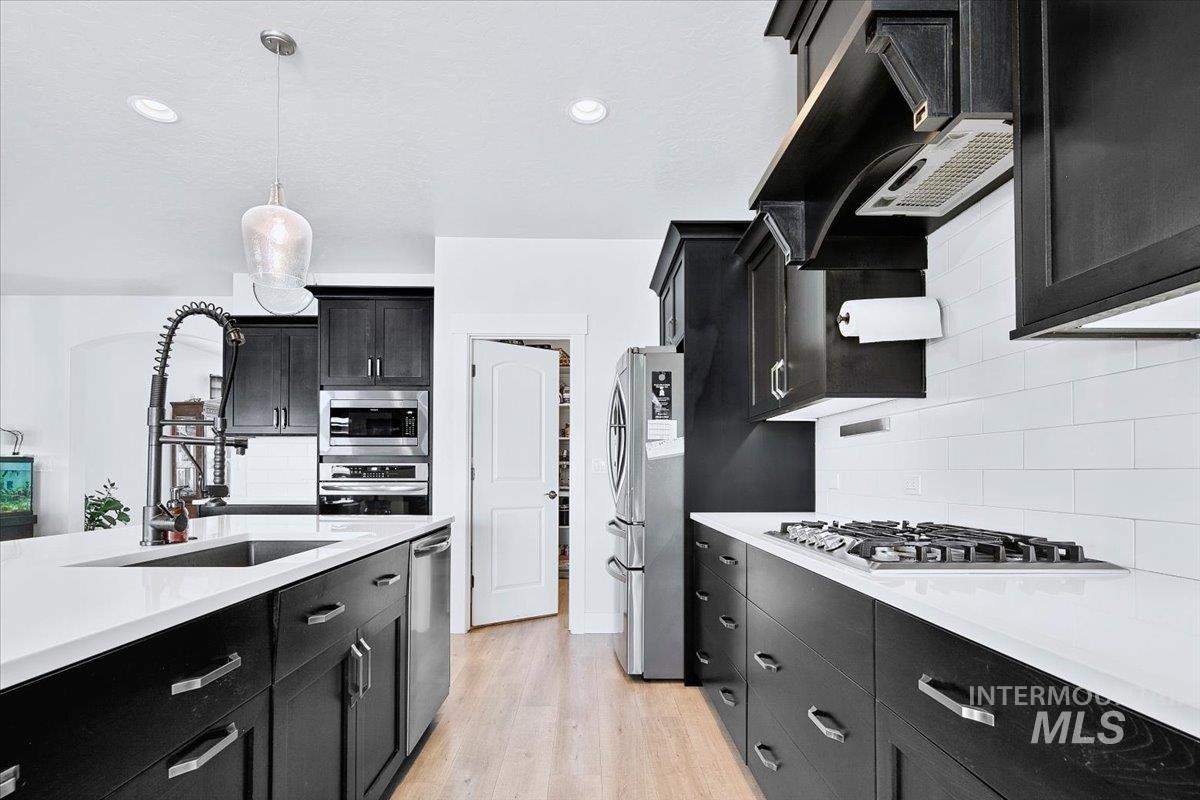 Modern kitchen featuring dark wood cabinetry, white countertops, stainless steel appliances, a gas cooktop, and a subway tile backsplash