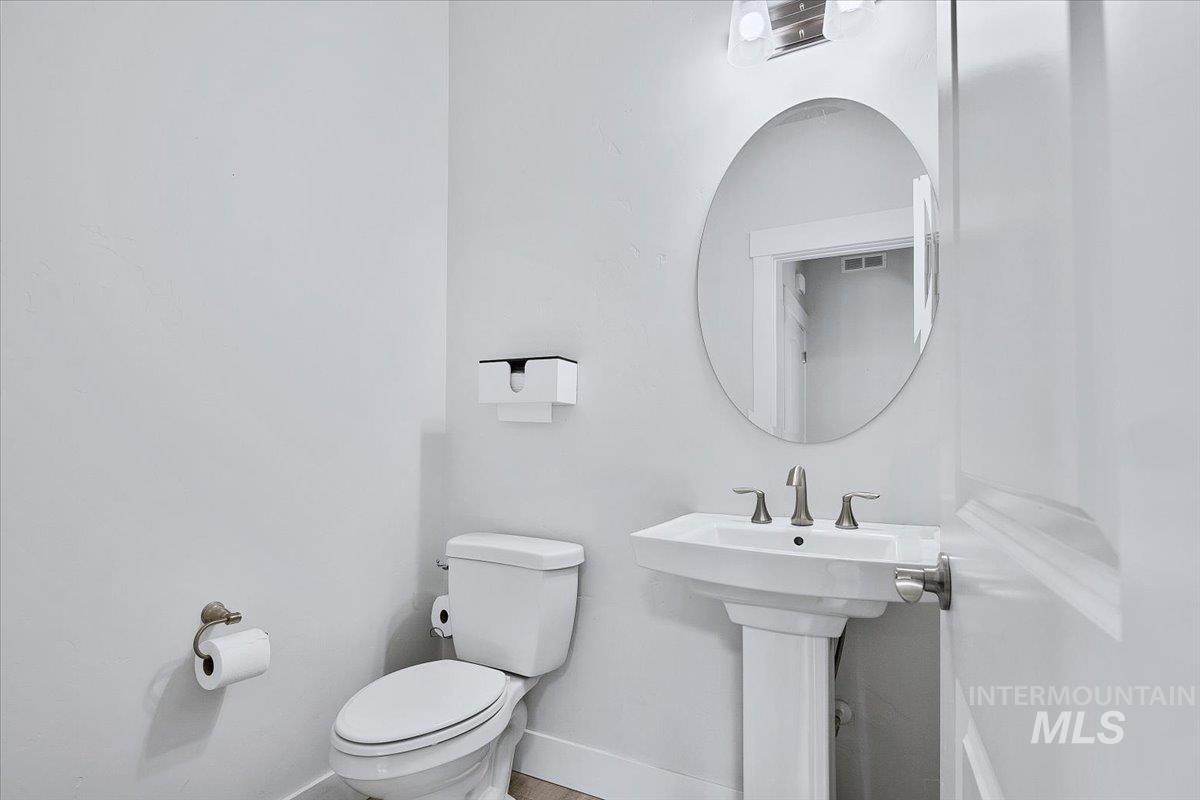 Pedestal sink with brushed nickel faucet, large round wall mirror, and modern vanity lighting