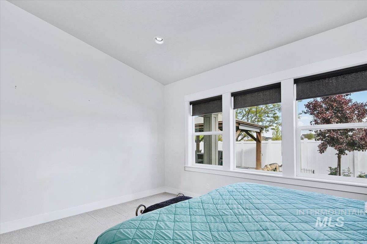 Bright room featuring three large windows with dark roller shades, overhead recessed lighting, and light carpet flooring