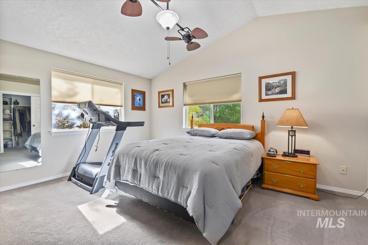 Bedroom with vaulted ceiling, carpet floors, a textured ceiling, a ceiling fan, and a closet