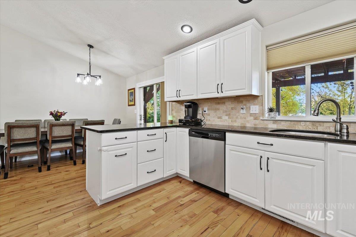 Kitchen featuring a peninsula, white cabinets, lofted ceiling, decorative light fixtures, and stainless steel dishwasher