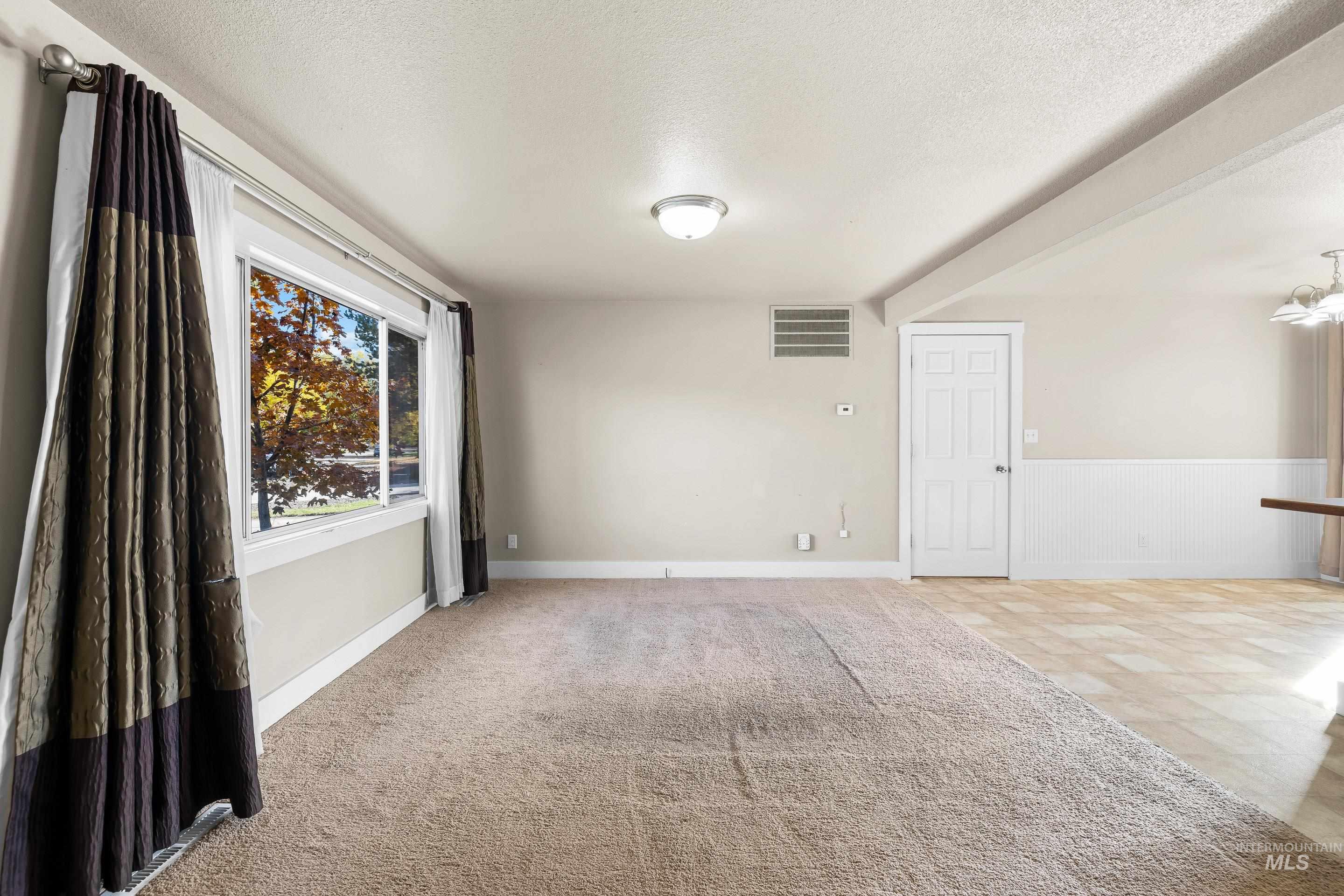 Spare room with a textured ceiling, light colored carpet, and wainscoting