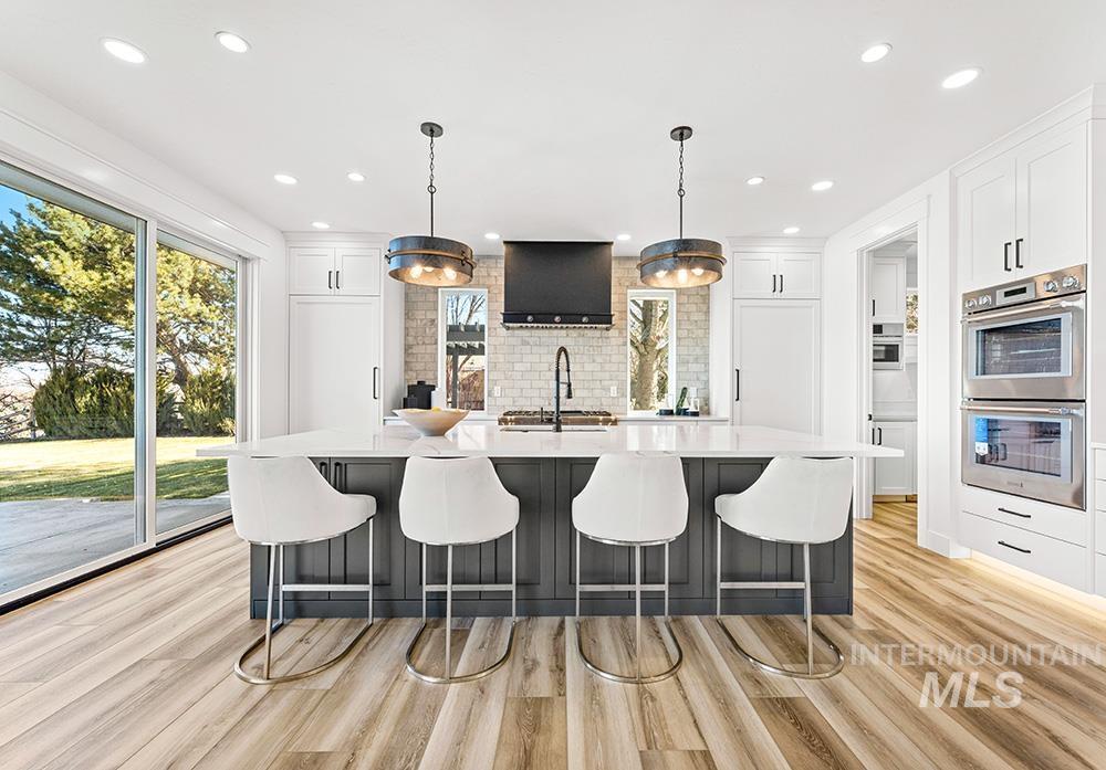 Kitchen with an island with sink, a kitchen breakfast bar, double oven, pendant lighting, and white cabinetry