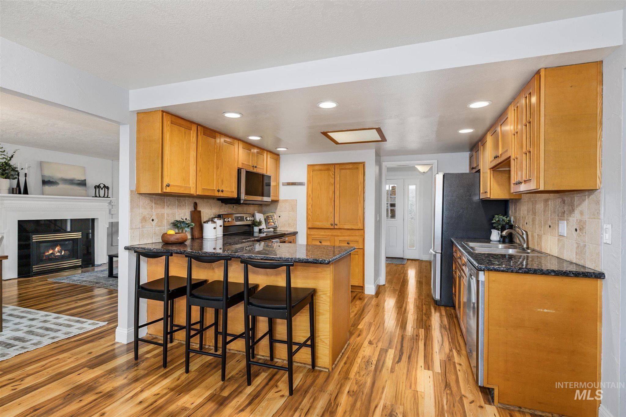 Kitchen with backsplash, a breakfast bar, a peninsula, a tile fireplace, and recessed lighting