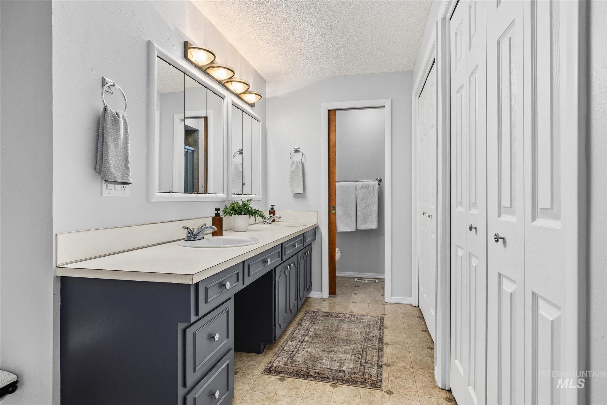 Full bath featuring a closet, double vanity, and a textured ceiling