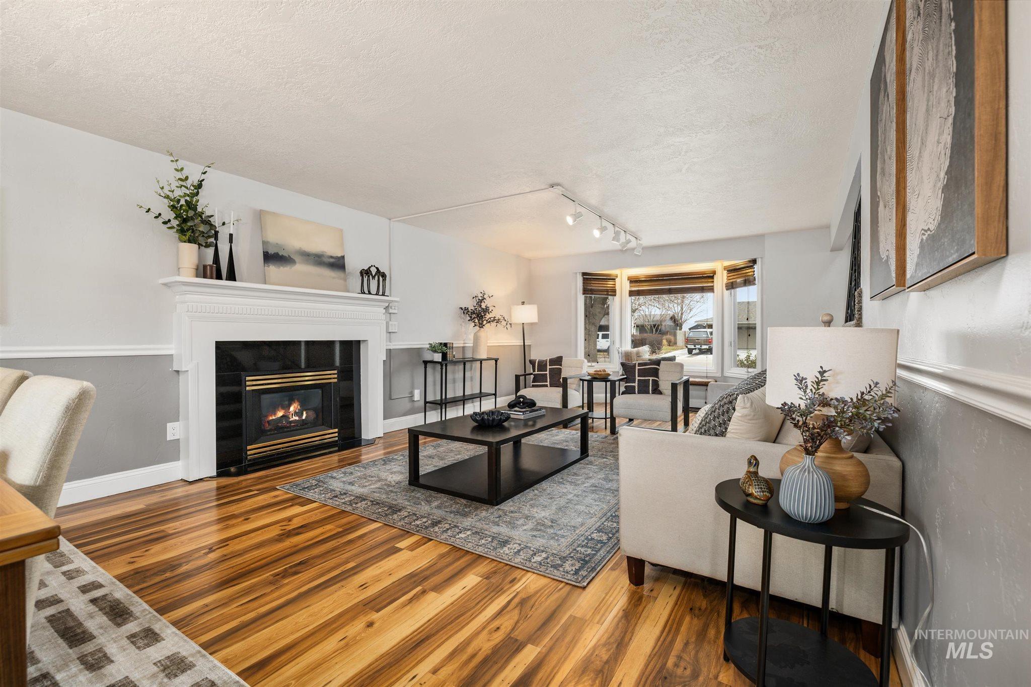 Living room with rail lighting, a textured ceiling, wood finished floors, and a tile fireplace