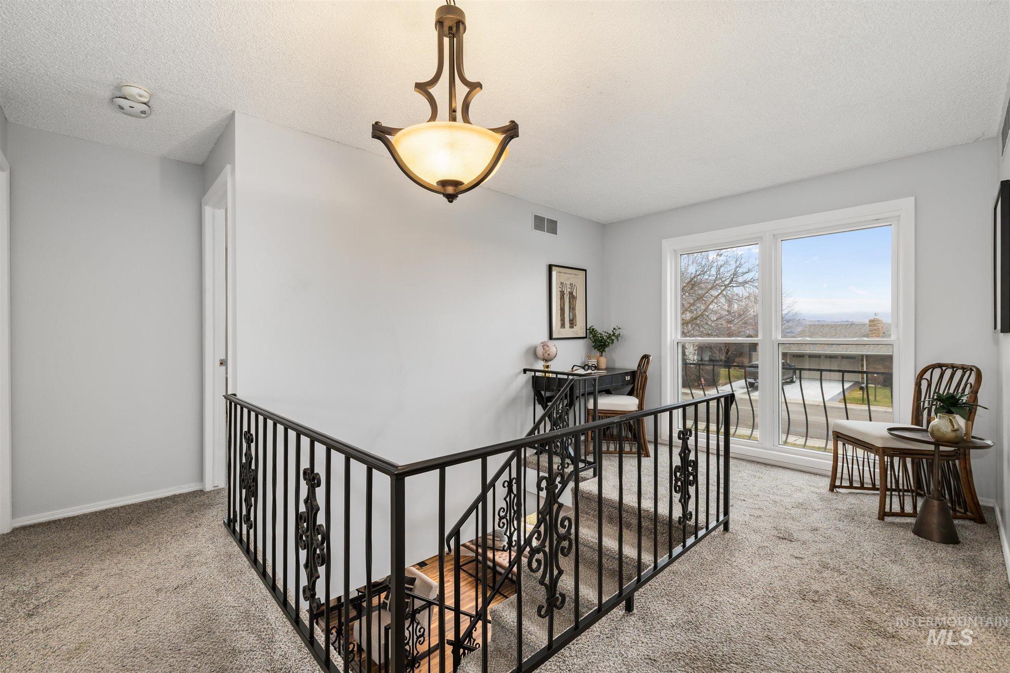 Hall with an upstairs landing, light colored carpet, and a textured ceiling