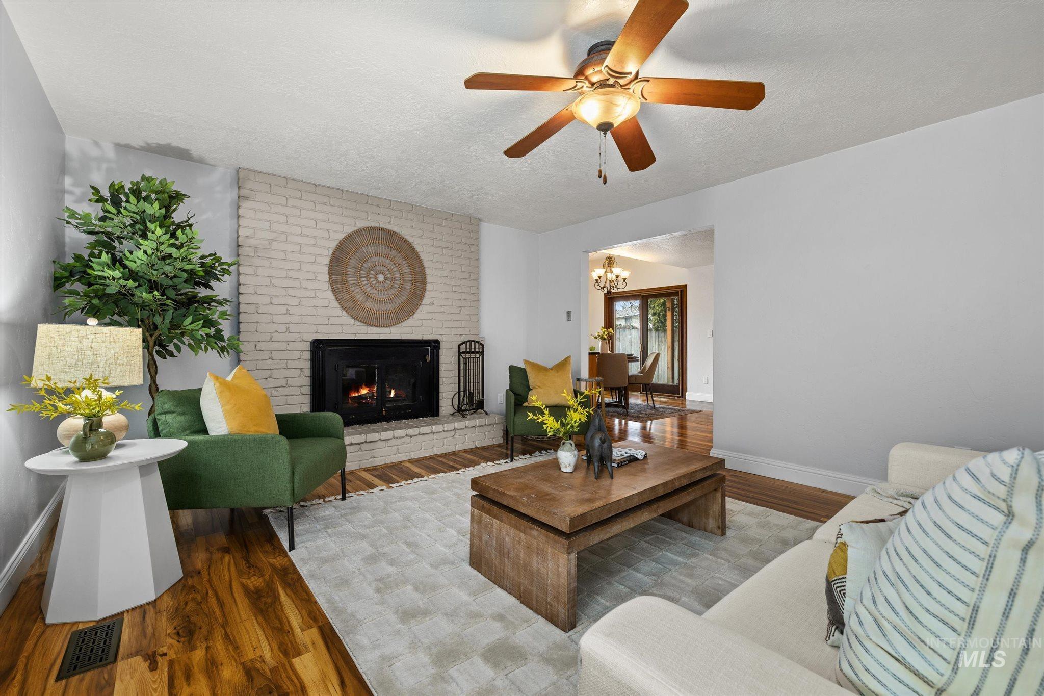 Living area featuring wood finished floors, a textured ceiling, a fireplace, a ceiling fan, and a chandelier