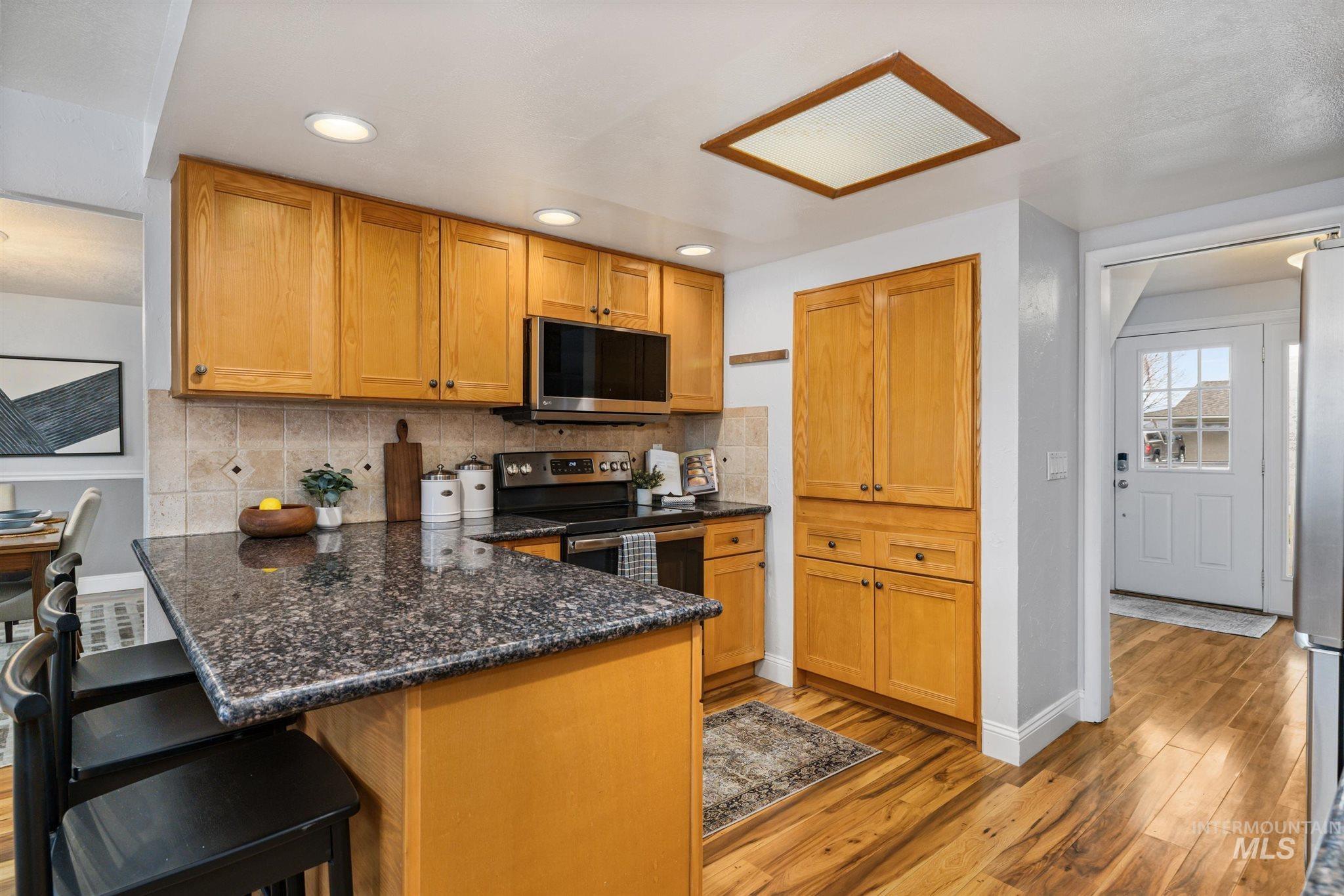 Kitchen featuring wood finish cabinets, stainless steel appliances, dark stone counters, a peninsula, and light wood-type flooring