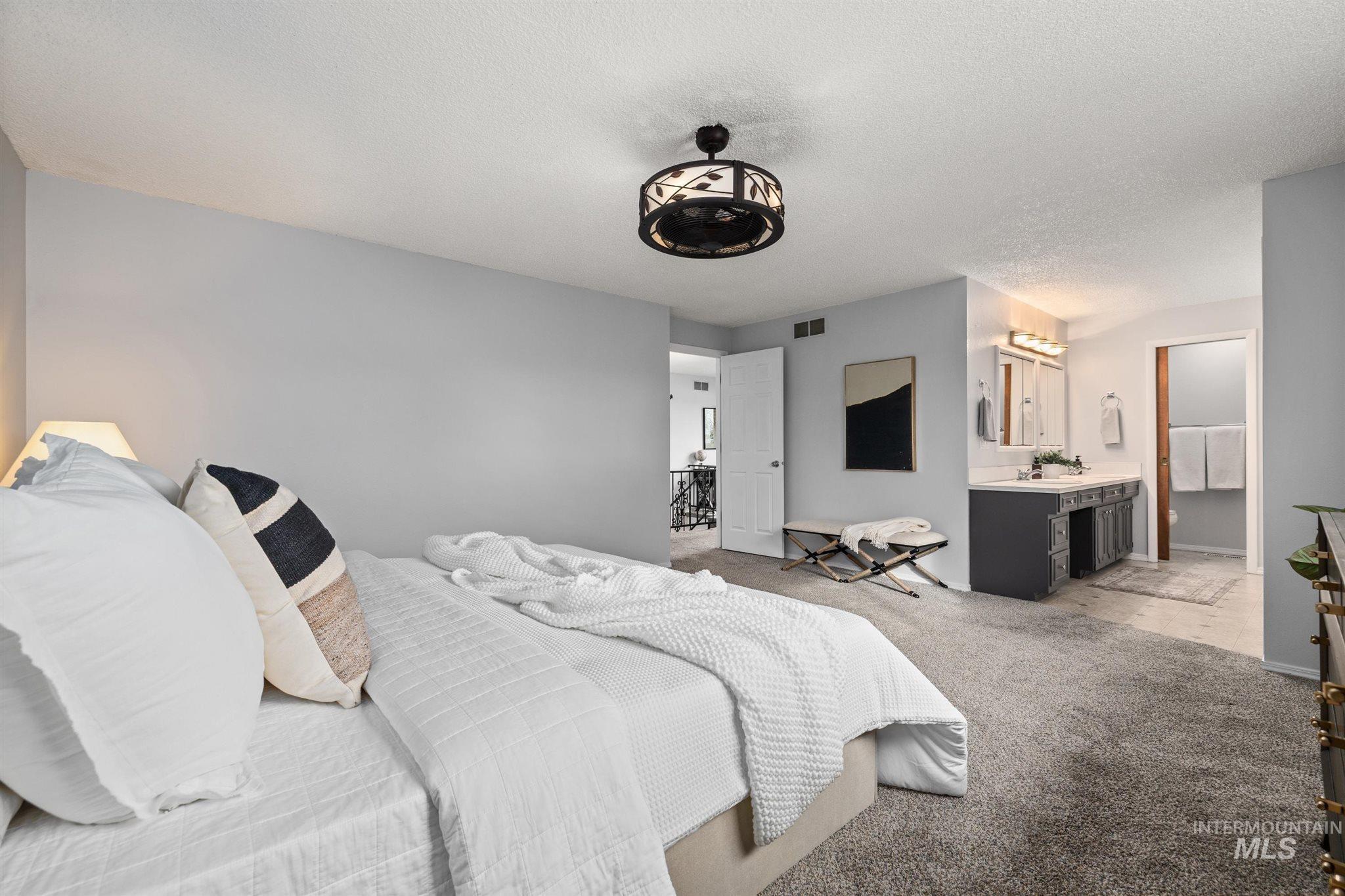 Bedroom with light carpet, a textured ceiling, and ensuite bath