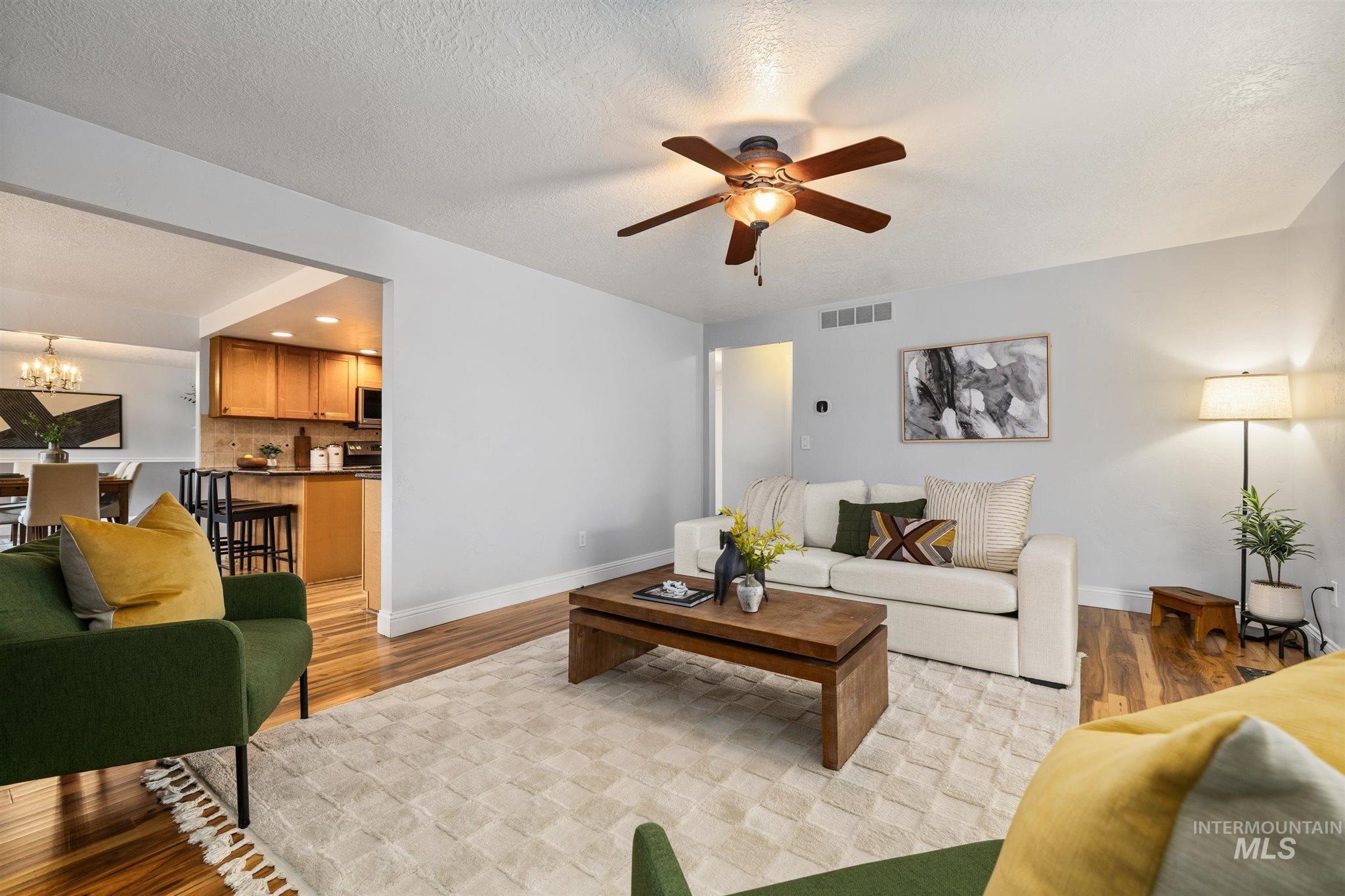 Living area featuring a ceiling fan, light wood-style flooring, a chandelier, and a textured ceiling
