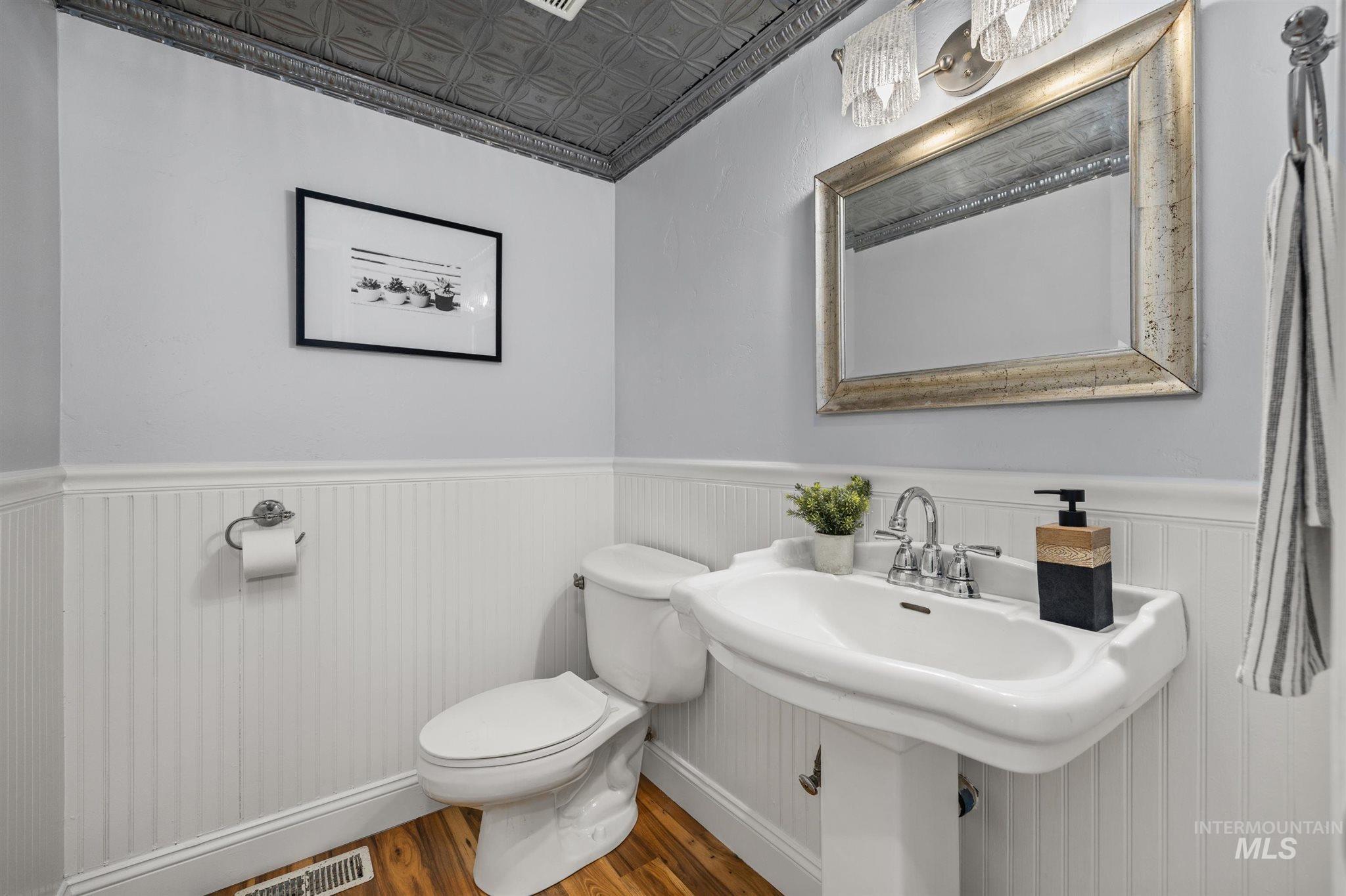 Half bathroom featuring an ornate ceiling, wood finished floors, a wainscoted wall, and ornamental molding