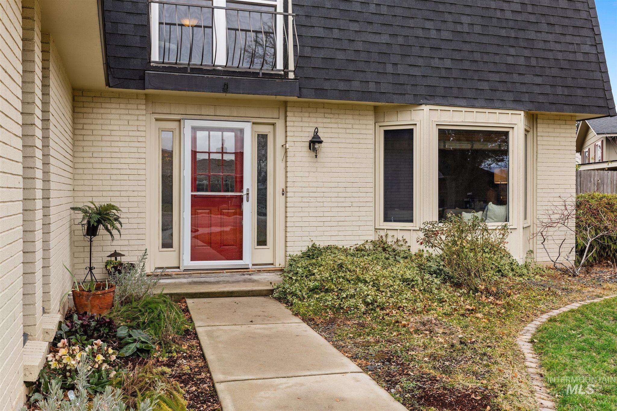 View of exterior entry with mansard roof, a shingled roof, and brick siding