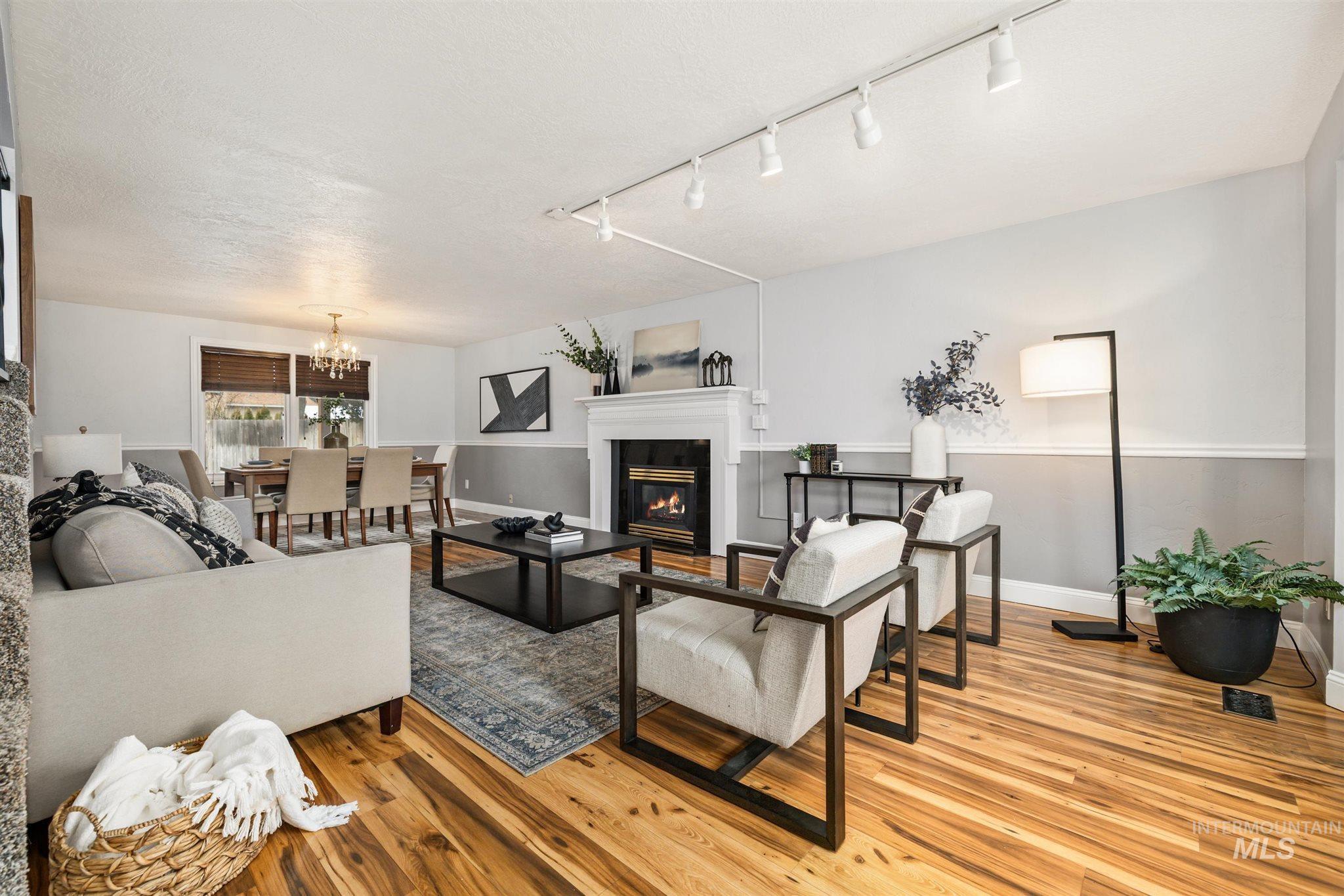 Living room featuring light wood-style flooring, a glass covered fireplace, a textured ceiling, and a chandelier