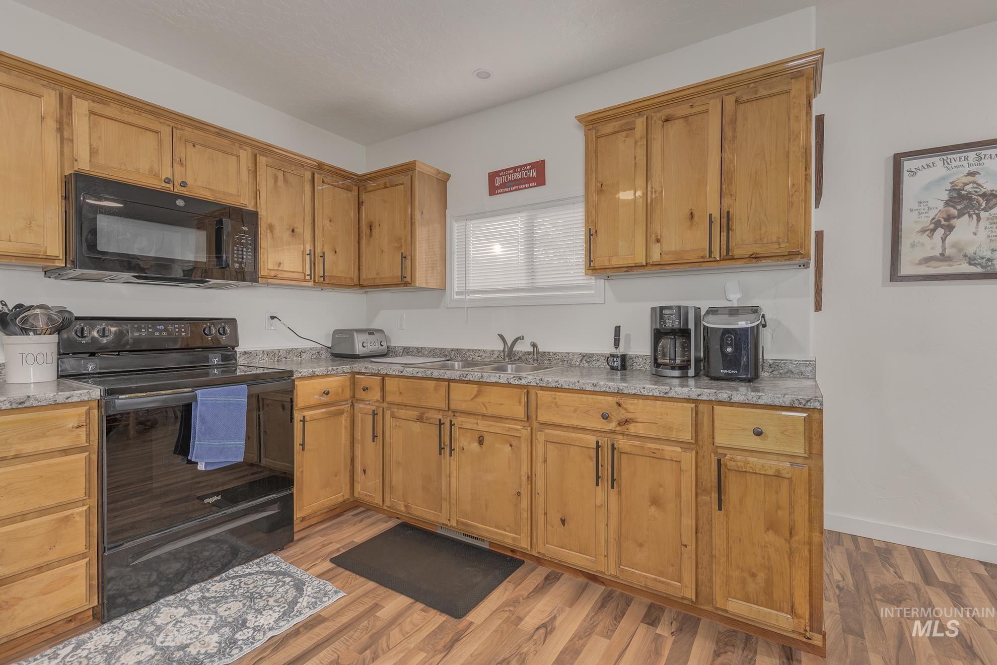 Kitchen with black appliances, light countertops, light wood-style flooring, and brown cabinets