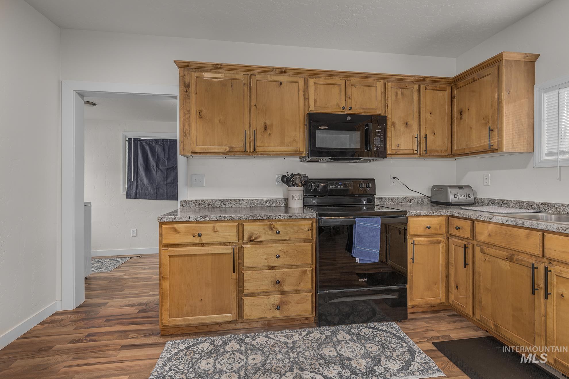 Kitchen featuring black appliances, dark wood-style floors, light countertops, and brown cabinetry