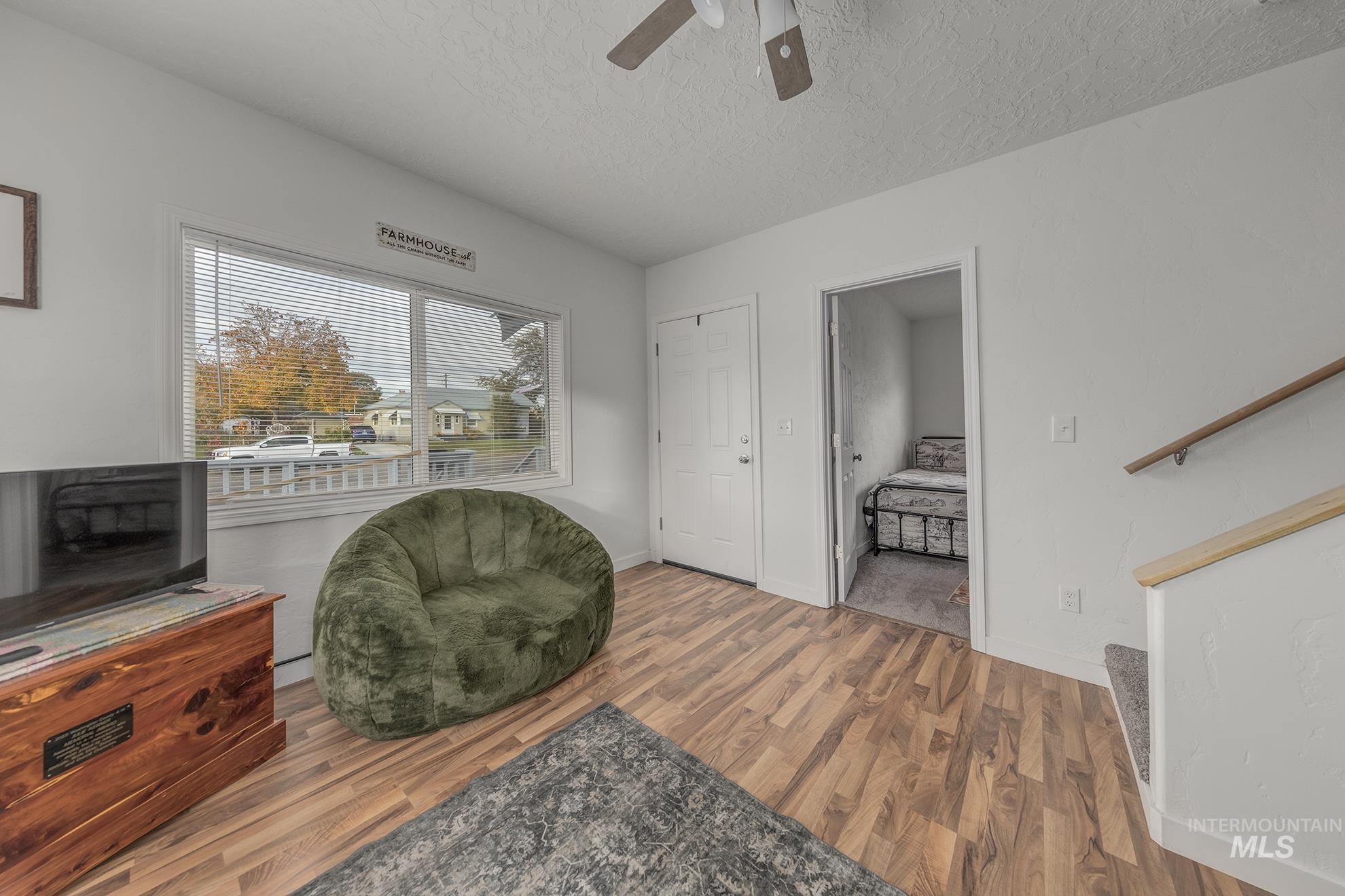 Living area with a textured ceiling, wood finished floors, ceiling fan, and stairs