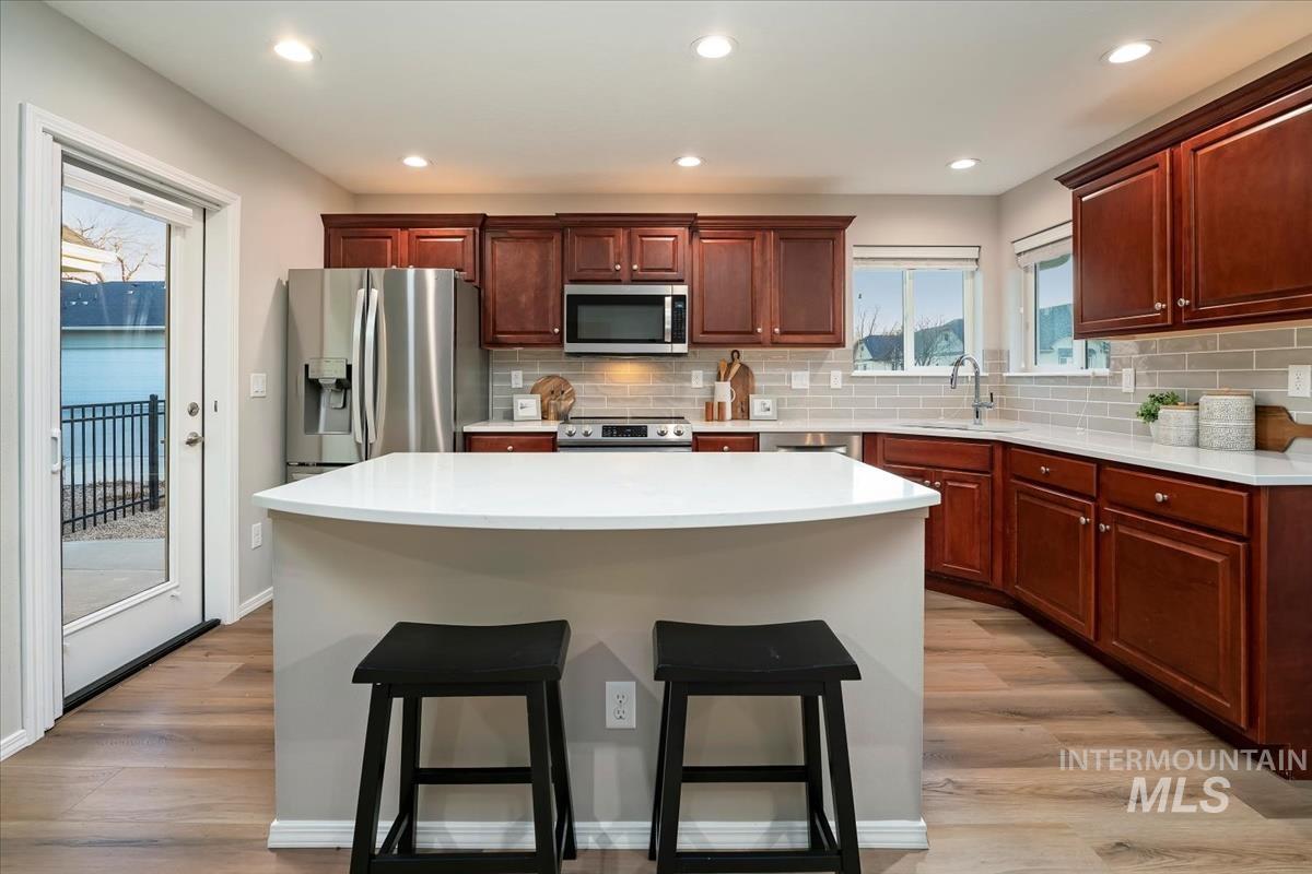 Kitchen featuring stainless steel appliances, a breakfast bar area, a center island, light wood-type flooring, and tasteful backsplash
