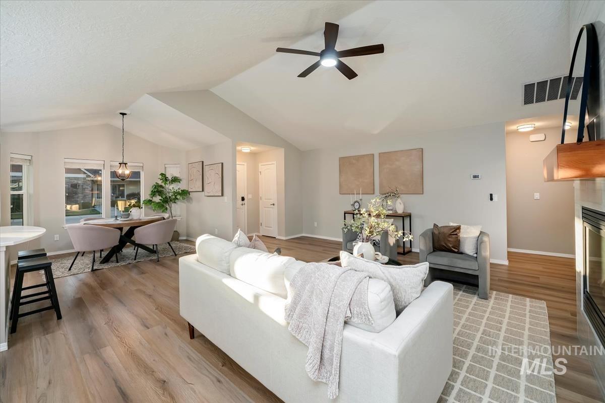 Living area with a tile fireplace, a ceiling fan, light wood-style flooring, vaulted ceiling, and a chandelier