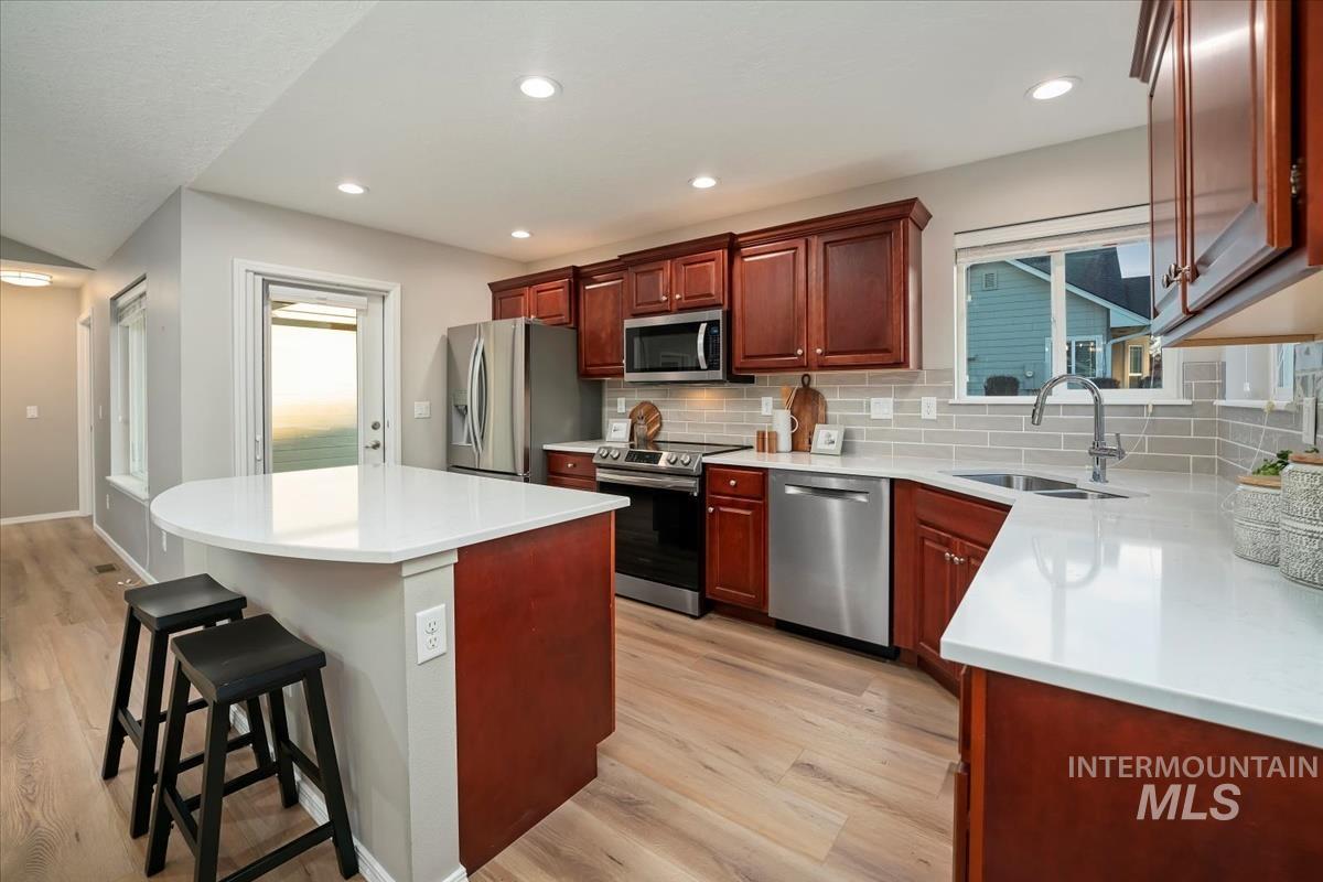 Kitchen featuring a breakfast bar, a center island, appliances with stainless steel finishes, light wood-type flooring, and recessed lighting