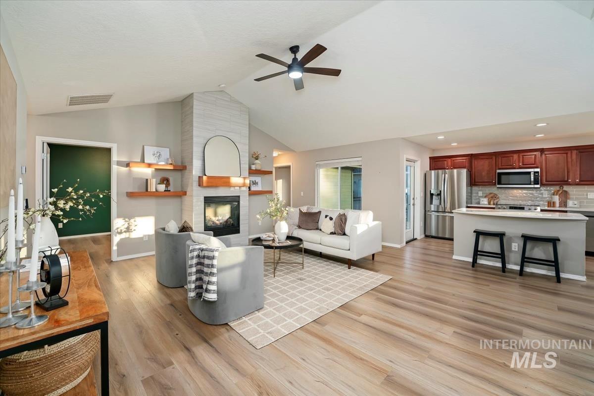 Living area with light wood finished floors, a large fireplace, ceiling fan, and high vaulted ceiling