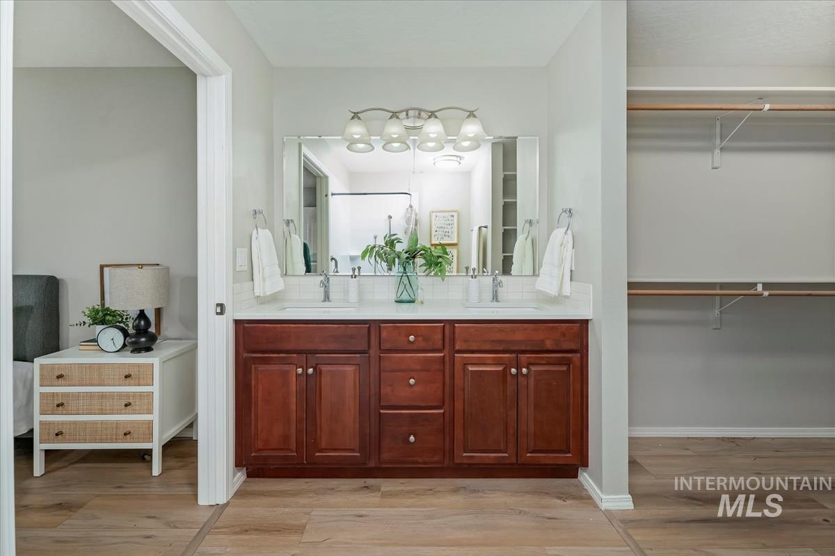 Full bath with a spacious closet, double vanity, and light wood-type flooring