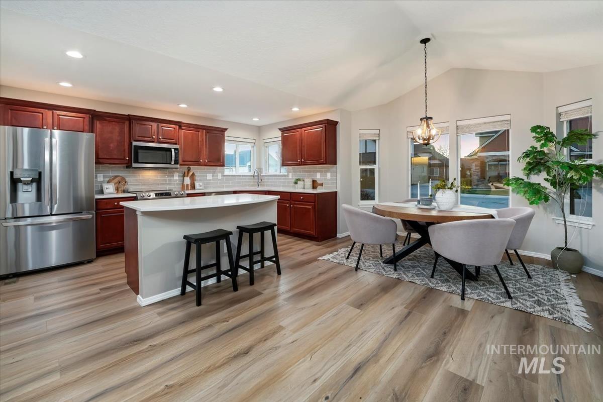 Kitchen with appliances with stainless steel finishes, a breakfast bar, a kitchen island, decorative light fixtures, and backsplash