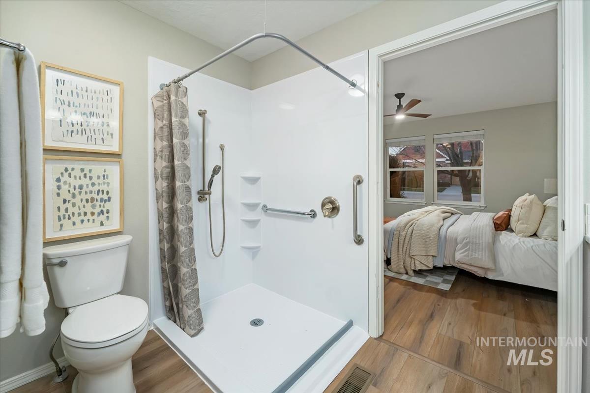 Ensuite bathroom featuring wood finished floors, a shower with curtain, and a ceiling fan