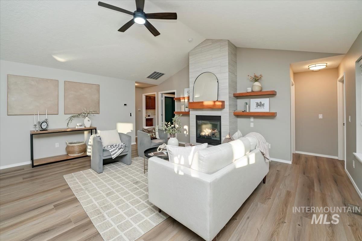Living room with a large fireplace, vaulted ceiling, light wood-style floors, and a ceiling fan
