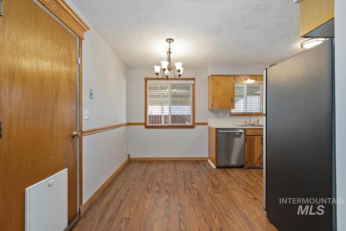 Kitchen featuring light countertops, appliances with stainless steel finishes, light wood finished floors, a chandelier, and pendant lighting