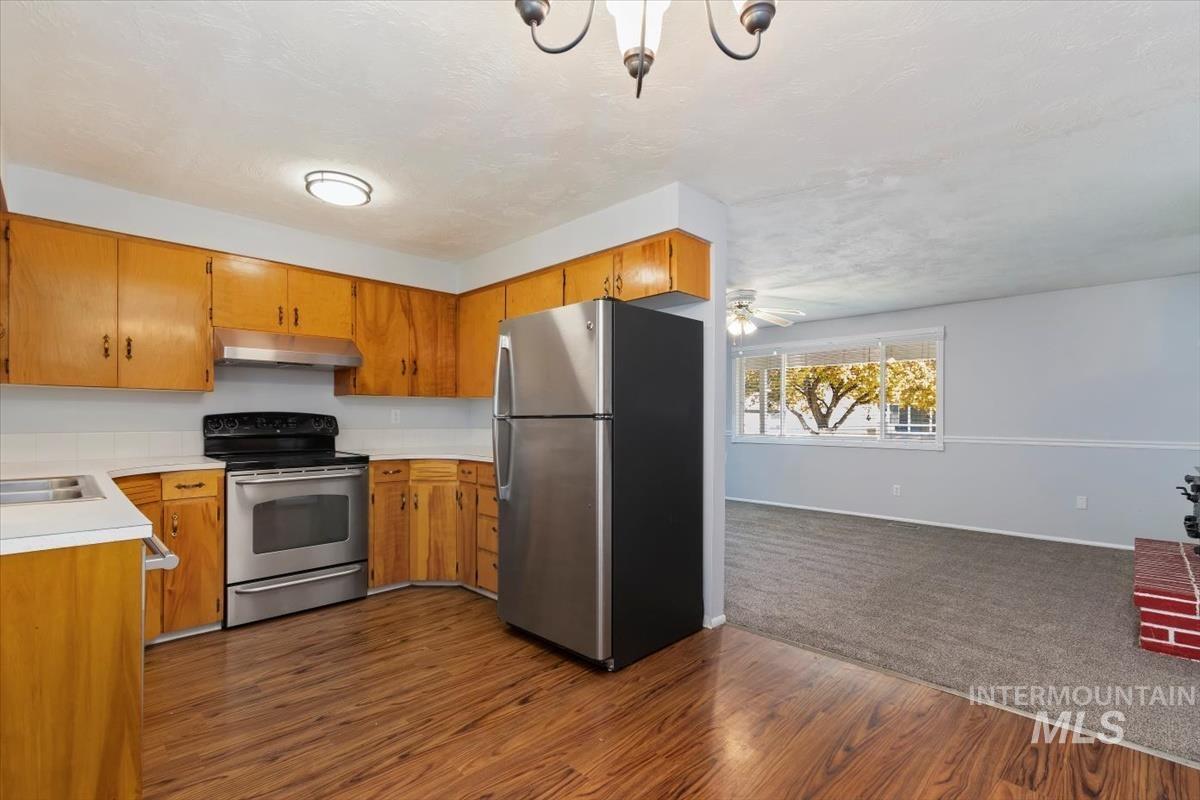 Kitchen featuring light countertops, stainless steel appliances, dark wood-style flooring, brown cabinetry, and under cabinet range hood