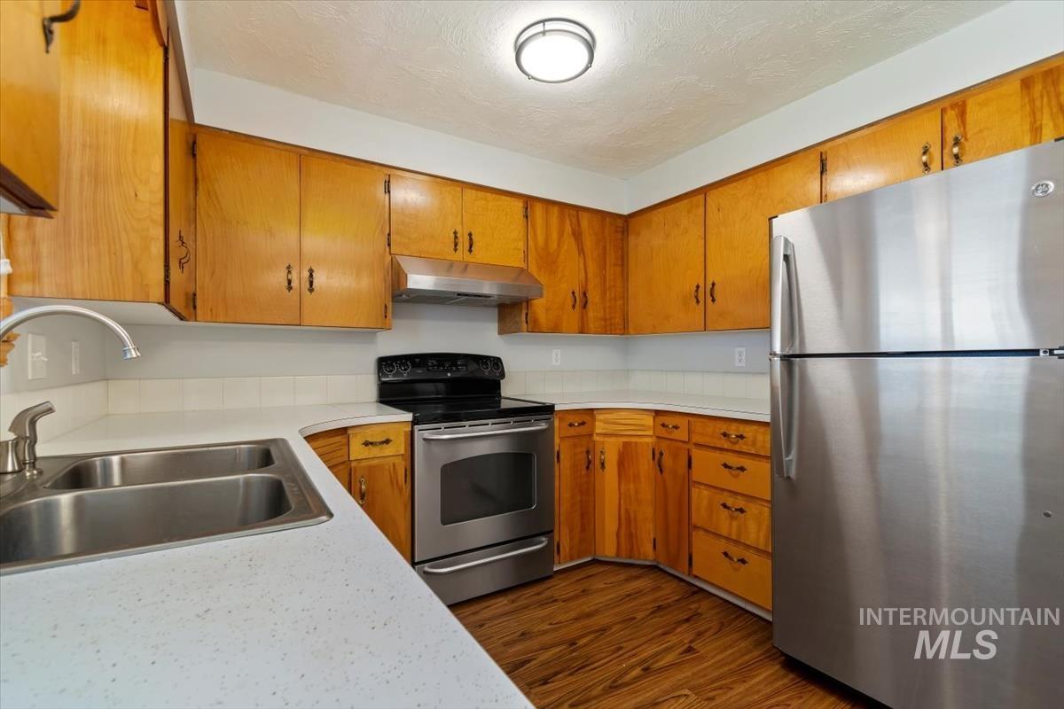 Kitchen with appliances with stainless steel finishes, light countertops, a textured ceiling, dark wood-style flooring, and under cabinet range hood