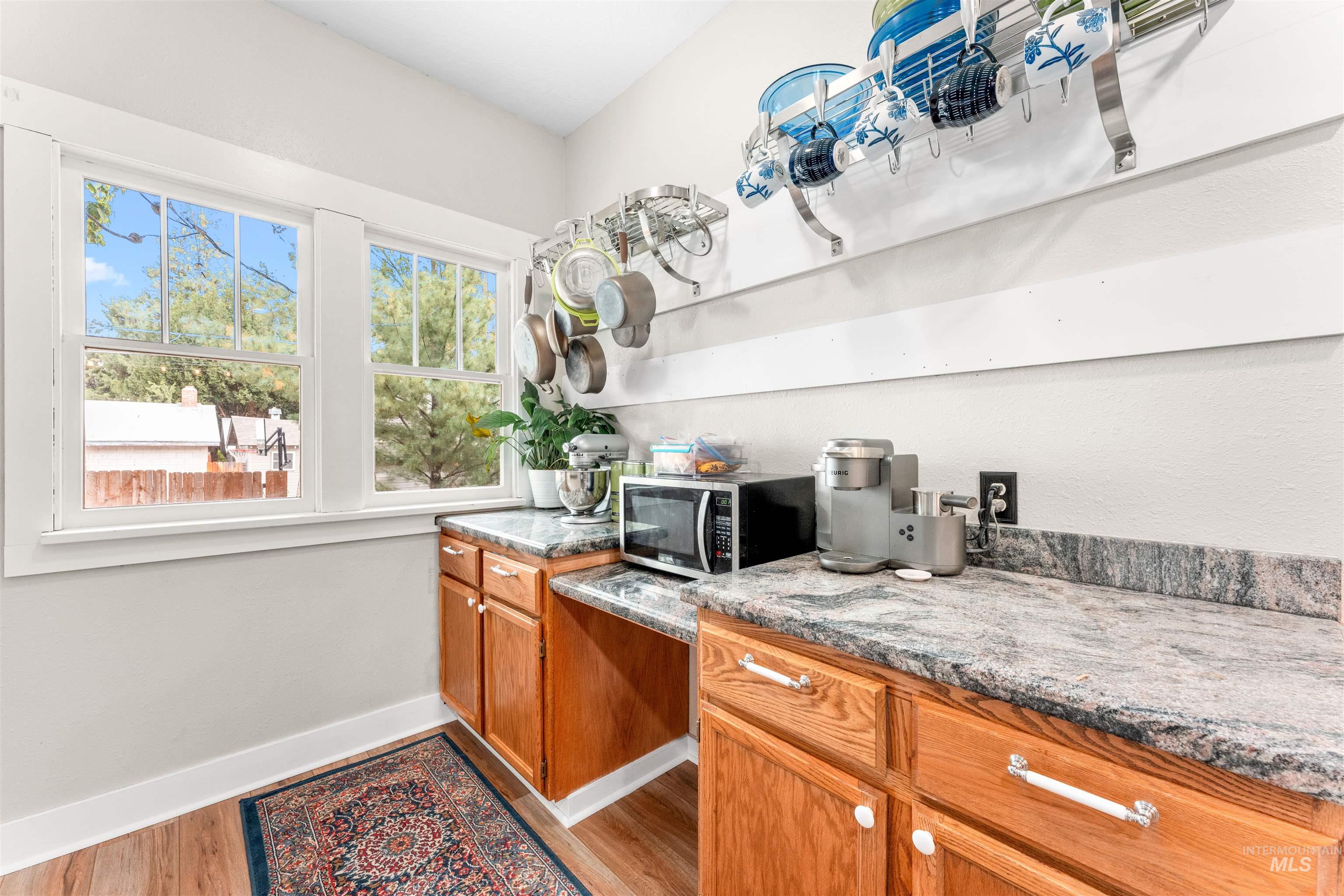 Kitchen featuring brown cabinets, stainless steel microwave, light stone countertops, and light wood-style flooring