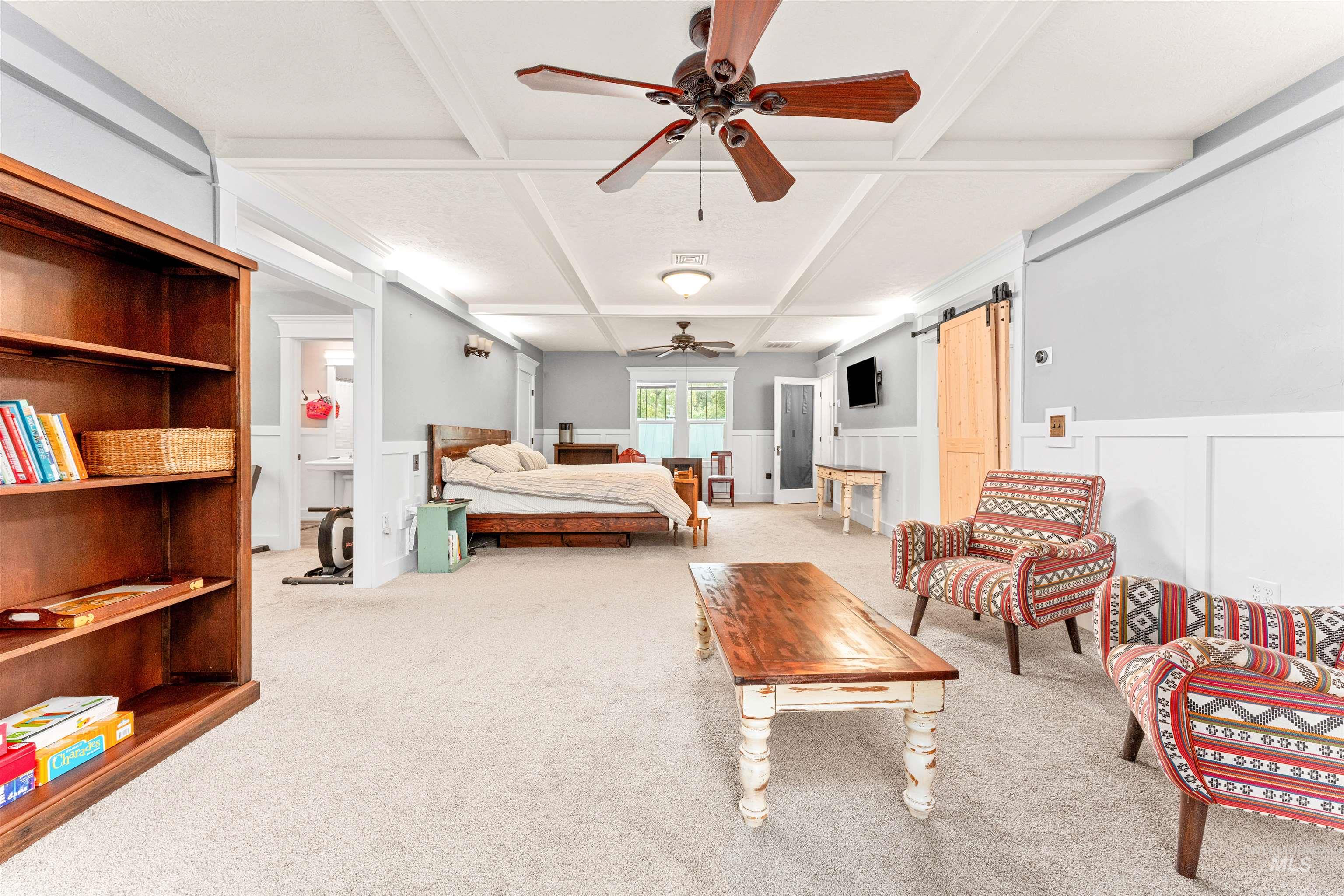 Primary Bedroom Suite with beamed ceiling, coffered ceiling, a barn door, wainscoting, and light colored carpet