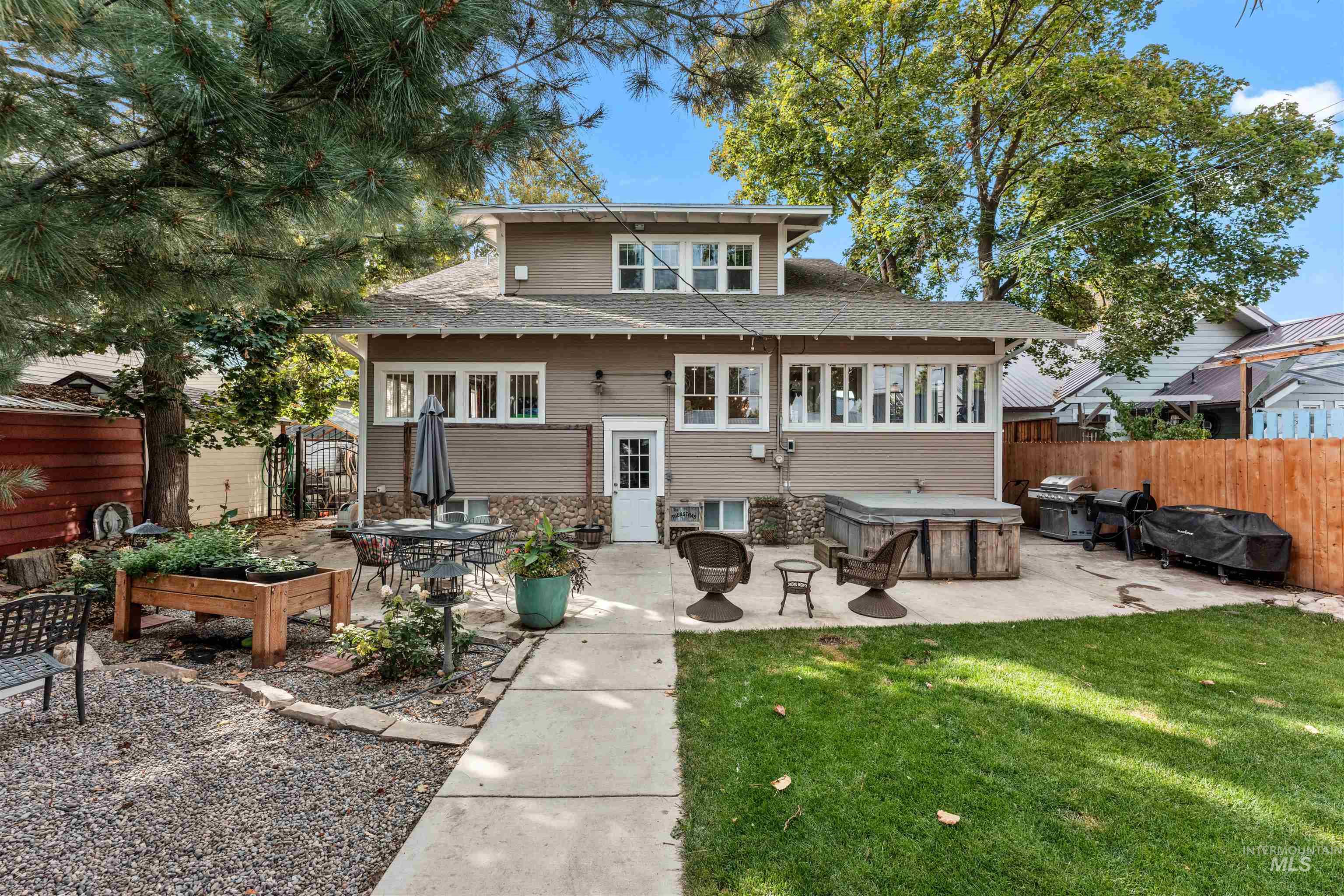 Rear view of house with a patio, roof with shingles, a fenced backyard, and a hot tub